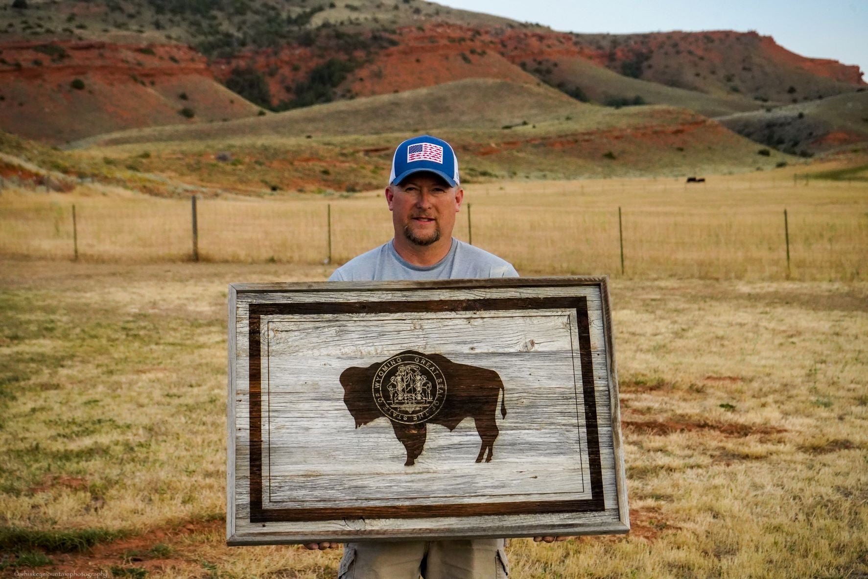 Owner of Wind River Outpost, Mike Strasser holds up a rustic Wyoming State Flag made of barnwood.