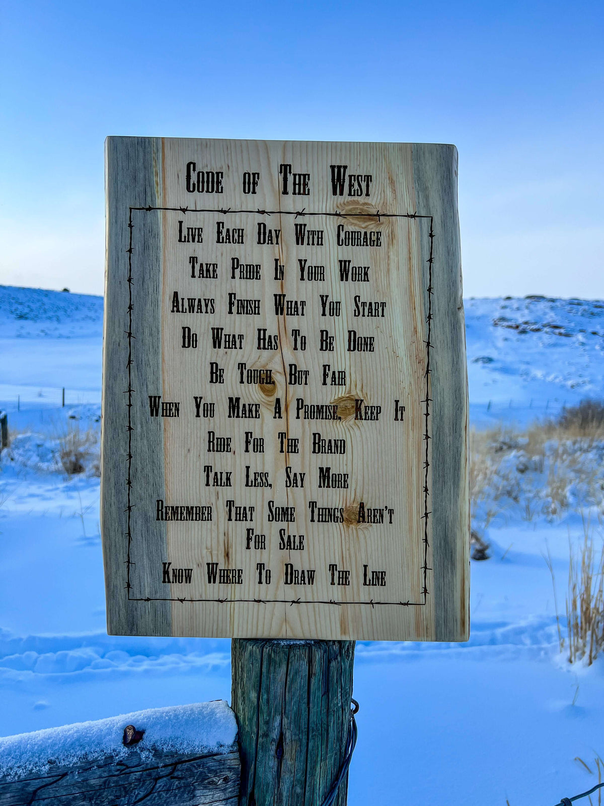 Code of the West wording laser engraved on pine, displayed on fence post in Wyoming landscape